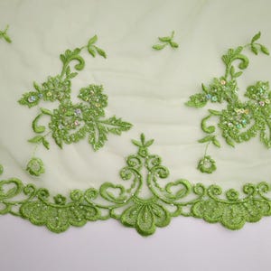 Puede incluir: Tela de encaje floral verde con lentejuelas. El encaje tiene un borde festoneado.