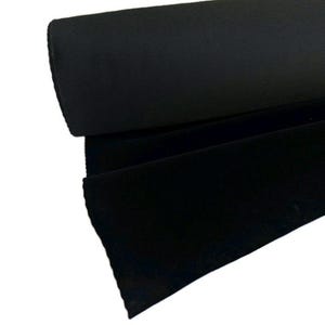 May include: A roll of solid black fabric featuring a dense, uniform weave. The material is tightly wound into a cylindrical shape, with a portion of the fabric unrolled to display the smooth, matte texture and consistent deep black color.
