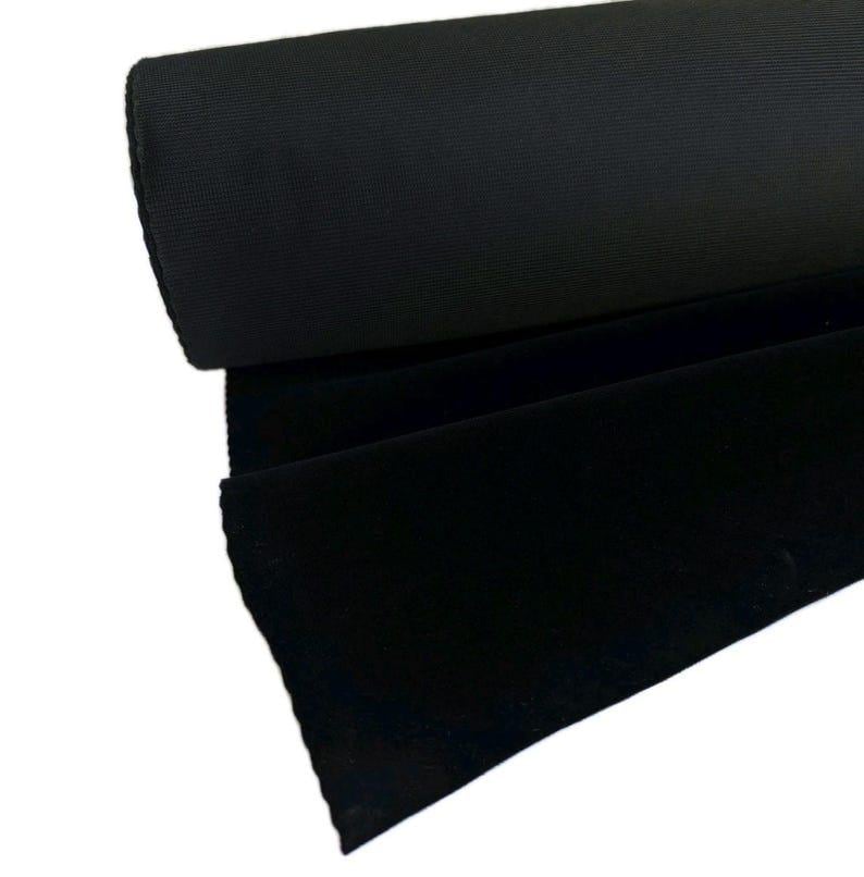 May include: A roll of solid black fabric featuring a dense, uniform weave. The material is tightly wound into a cylindrical shape, with a portion of the fabric unrolled to display the smooth, matte texture and consistent deep black color.