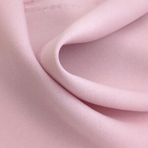 Puede incluir: Primer plano de una tela rosa p&aacute;lido con una sutil textura tejida. La tela est&aacute; drapeada en pliegues suaves, creando sombras y reflejos que resaltan su superficie lisa. La apariencia general sugiere un textil delicado y lujoso.