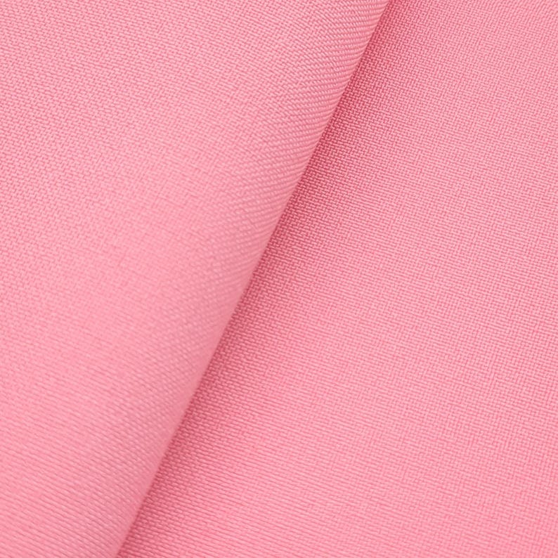 Puede incluir: Primer plano de un trozo de tela rosa doblada. La tela tiene una textura sutil y un ligero brillo, con un pliegue diagonal que crea un contraste de luz y sombra. El color es un rosa suave y apagado.