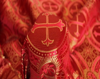 Może przedstawiać: Zbliżenie czerwonej szaty religijnej ze złotym wzorem krzyża. Tkanina ma szczegółowy wzór ze złotymi akcentami. Krzyż jest obrysowany złotem i ma dekoracyjne zdobienia.