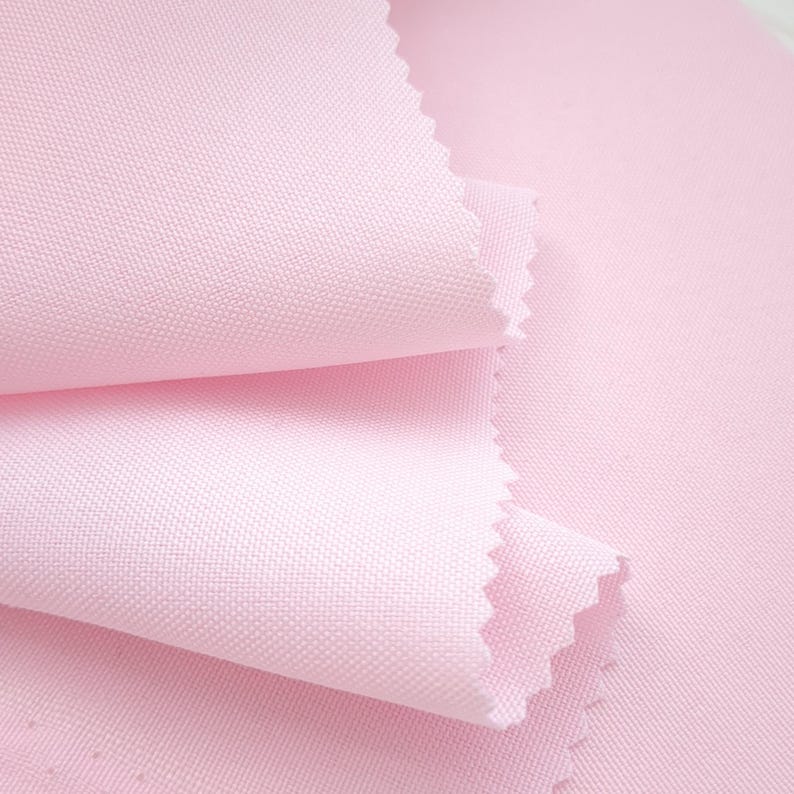 Puede incluir: Primer plano de una pila de tela rosa claro con un tejido texturizado. Los bordes de la tela est&aacute;n cortados con un patr&oacute;n en zigzag. La tela est&aacute; doblada sobre s&iacute; misma, mostrando la textura y las variaciones de color.