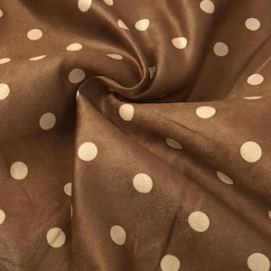 May include: A brown fabric with a repeating pattern of off-white polka dots. The material is gathered in the center, creating soft folds and shadows that highlight the smooth, matte texture of the textile and the consistent circular design.