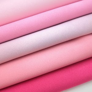 Puede incluir: Primer plano de varias muestras de tela rosa, con tonos que van desde el rosa p&aacute;lido hasta el fucsia vibrante. La tela parece ser de algod&oacute;n finamente tejido o un material similar, con un ligero brillo.