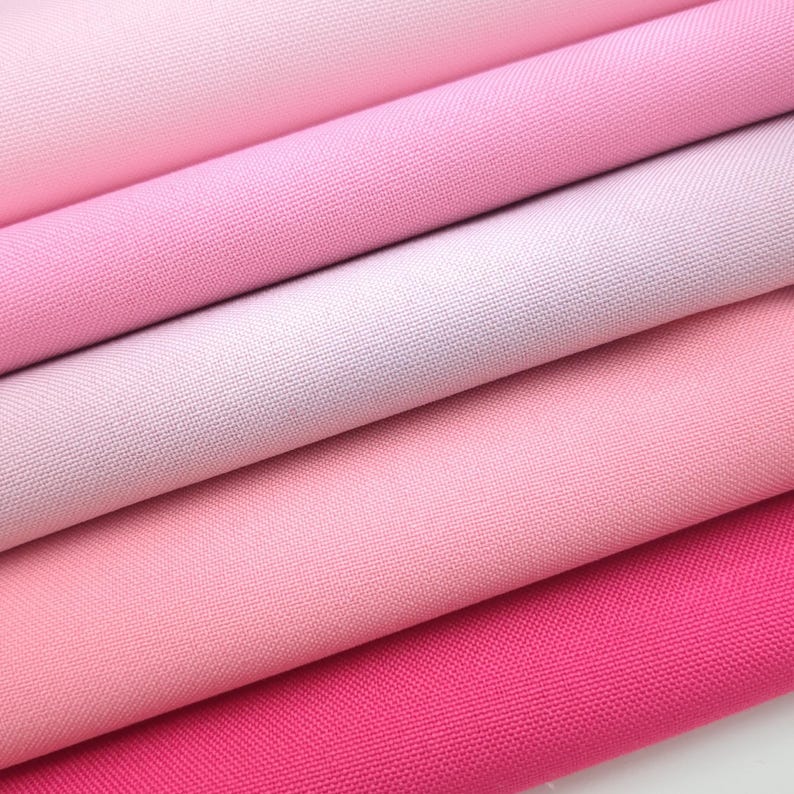 Puede incluir: Primer plano de varias muestras de tela rosa, con tonos que van desde el rosa p&aacute;lido hasta el fucsia vibrante. La tela parece ser de algod&oacute;n finamente tejido o un material similar, con un ligero brillo.