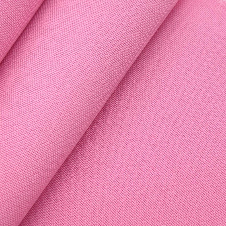 Puede incluir: Primer plano de una secci&oacute;n doblada de tela de lona rosa. La tela tiene una textura densamente tejida y los pliegues crean sombras. El color es un rosa vibrante y liso.