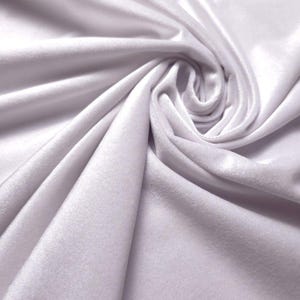 May include: A solid white fabric with a soft, velvet-like texture, featuring deep folds and a swirling drape that creates light and shadow across the surface. The material has a subtle sheen and a dense, plush pile appearance throughout.