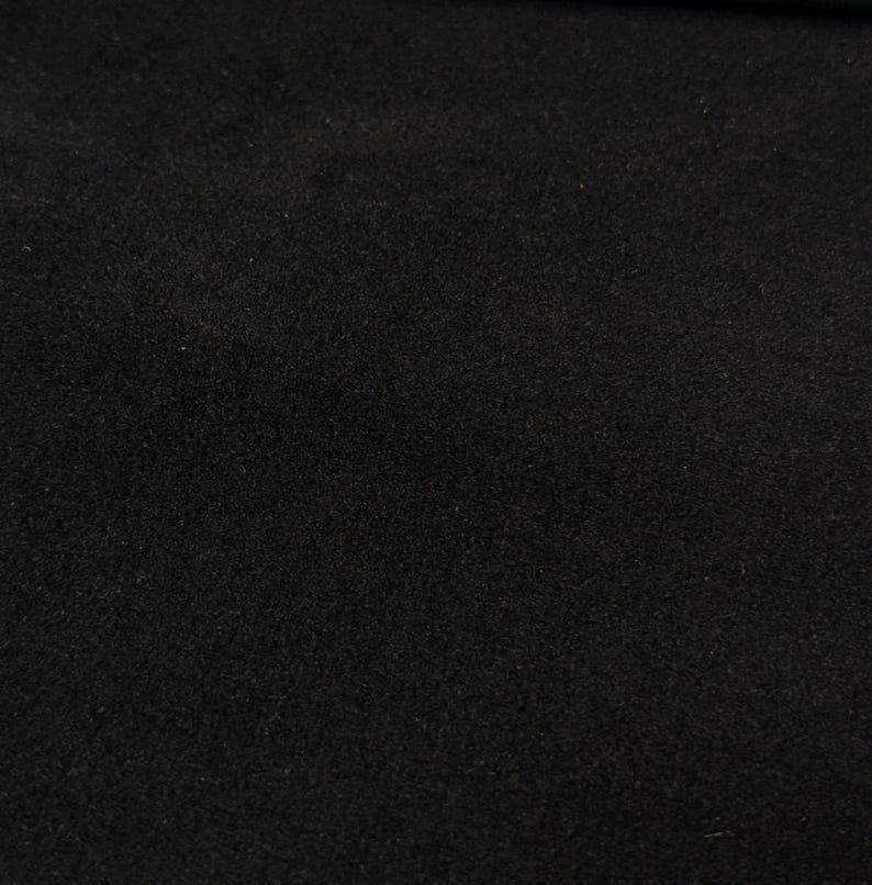 May include: A solid black fabric surface with a fine, uniform, and slightly textured matte finish. The material appears dense and opaque, covering the entire frame with a consistent dark tone and a subtle, granular visual quality.