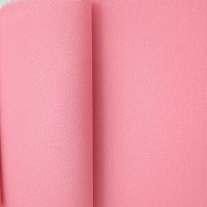 Puede incluir: Primer plano de un rollo de tela rosa. La tela tiene una textura tejida y un color rosa claro liso. El rollo est&aacute; parcialmente desenrollado, revelando la textura y el color del material.