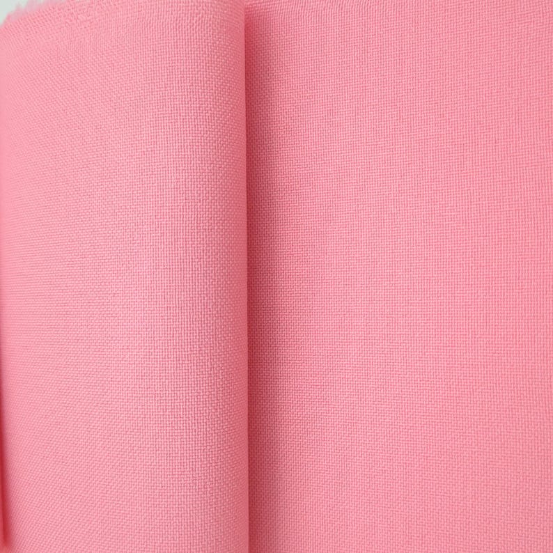Puede incluir: Primer plano de un rollo de tela rosa. La tela tiene una textura tejida y un color rosa claro liso. El rollo est&aacute; parcialmente desenrollado, revelando la textura y el color del material.