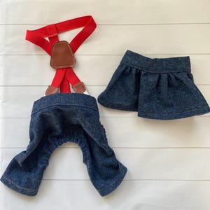 May include: A dark blue denim overall set featuring red elastic braces with brown leather-look accents and a matching dark blue denim pleated skirt. The overalls have a gathered waist and leg openings, while the skirt has a simple waistband.