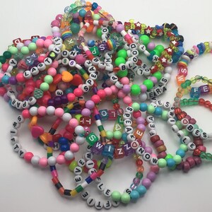 Puede incluir: Un mont&oacute;n de pulseras de cuentas de colores con cuentas de letras que deletrean palabras como "Speak", "Love", "Fifty", "Era", "Best", "Swizzle", "Even" y "Ftie".