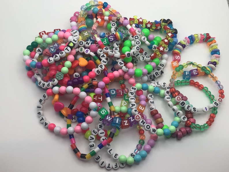 Puede incluir: Un mont&oacute;n de pulseras de cuentas de colores con cuentas de letras que deletrean palabras como "Speak", "Love", "Fifty", "Era", "Best", "Swizzle", "Even" y "Ftie".