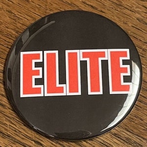 Puede incluir: Un botón negro y blanco con la palabra "ELITE" en letras rojas.