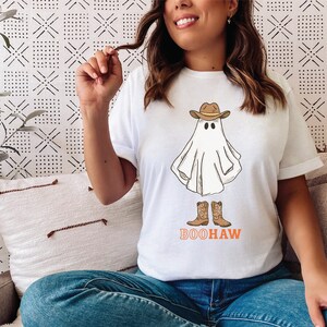 May include: White t-shirt with a ghost wearing a cowboy hat and boots. The text "BOOHAW" is printed below the ghost.