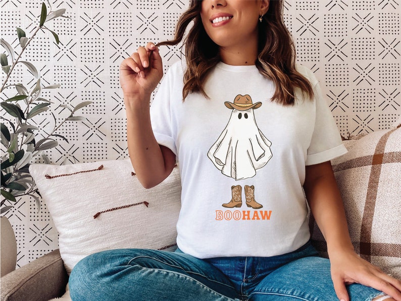May include: White t-shirt with a ghost wearing a cowboy hat and boots. The text "BOOHAW" is printed below the ghost.