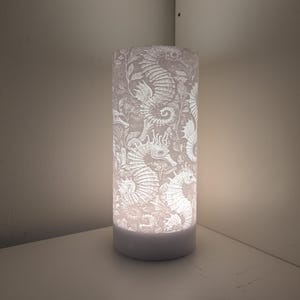 May include: White table lamp with a cylindrical shade featuring a white seahorse design.