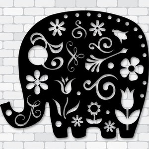 Puede incluir: Arte de pared negro con forma de elefante con intrincados recortes florales. El diseño presenta varios patrones de flores y espirales, creando una pieza decorativa y artística. El elefante está sobre un fondo de pared de ladrillos blancos.
