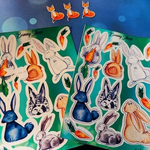 Könnte beinhalten: Zwei Blätter mit Aufklebern, die Aquarell-Illustrationen von Kaninchen mit Karotten zeigen. Die Aufkleber befinden sich auf einem türkisfarbenen Hintergrund mit dem Text "Bunny Sheet" oben auf jedem Blatt.