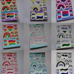 Könnte beinhalten: Neun verschiedene Aufkleberbögen mit verschiedenen Pride-Flaggen, darunter die Regenbogen-, Bi-, Transgender-, Pansexual- und Genderfluid-Flaggen. Jedes Blatt enthält ein Herz, einen Regenbogen und Streifen in den Farben der entsprechenden Flagge.