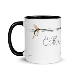 Op de afbeelding: Witte keramische koffiemok met een zwarte rand en handvat. De mok heeft een zwart-witte illustratie van een vliegenvislood met de tekst "Just Add Coffee".