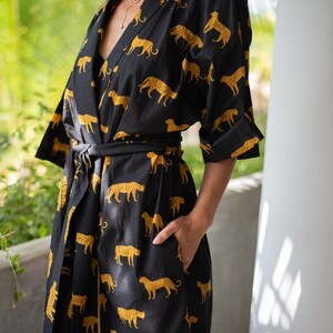 May include: A black and gold kimono robe with a leopard print pattern. The robe has a long sleeve and a tie belt.