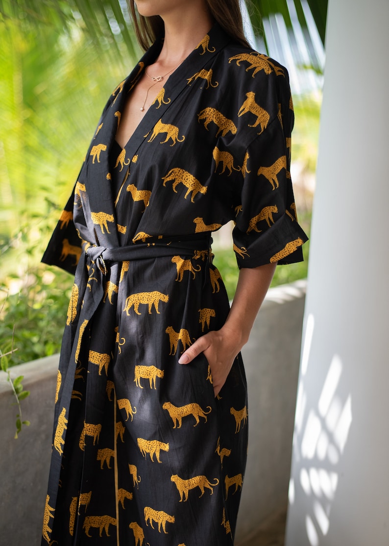 May include: A black and gold kimono robe with a leopard print pattern. The robe has a long sleeve and a tie belt.
