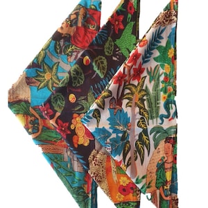 May include: Three triangular fabric napkins with colourful patterns. The napkins feature a jungle theme with vibrant colours, including green, blue, red, yellow, and orange. The patterns include tropical plants, animals, and people.