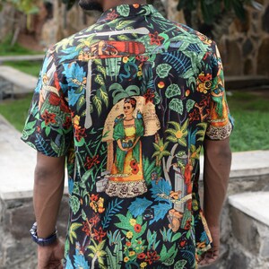May include: Short-sleeved button-down shirt with a vibrant, colorful print. The black shirt features a botanical design with images of a woman, plants, and animals. The shirt is paired with blue jeans.