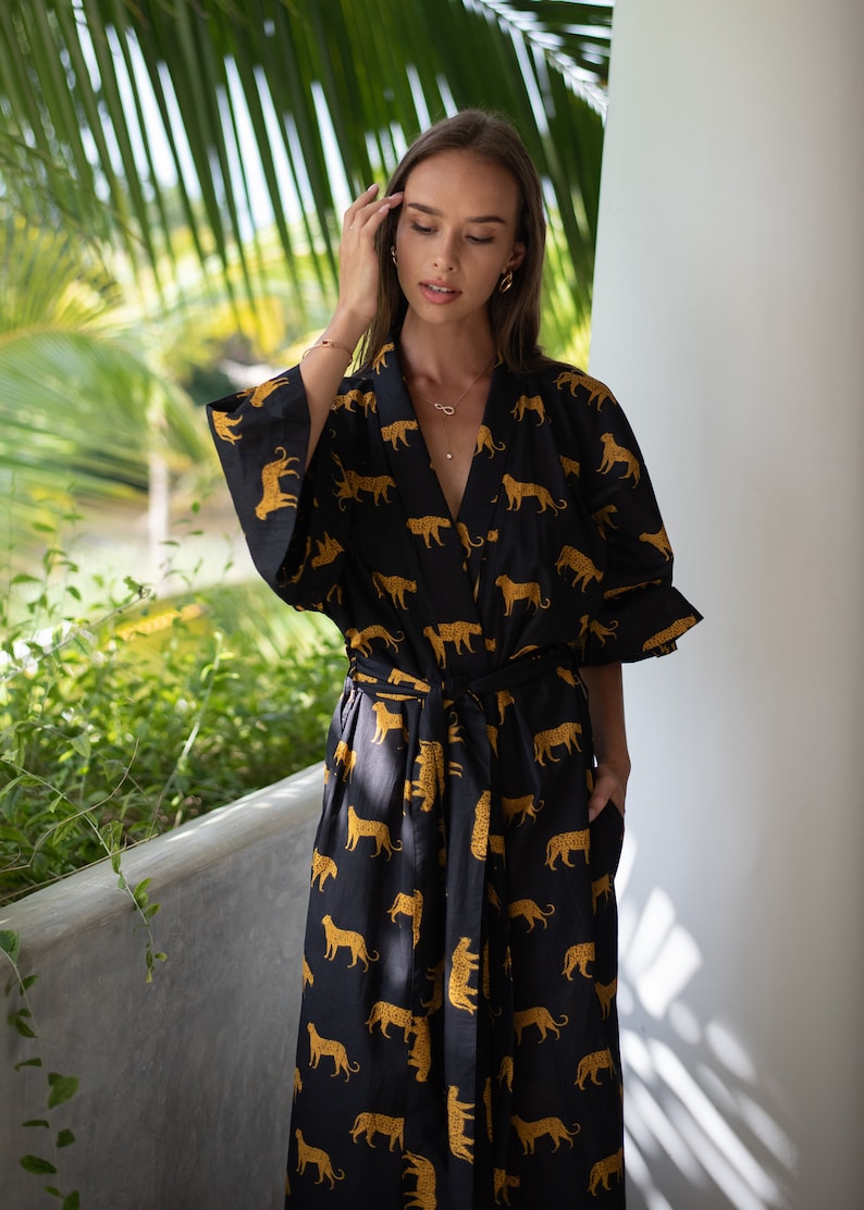 May include: A long black and gold robe with a leopard print. The robe has a tie belt and long sleeves.