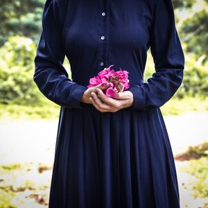 May include: A woman in a dark blue dress holds a bouquet of pink flowers in her hands.