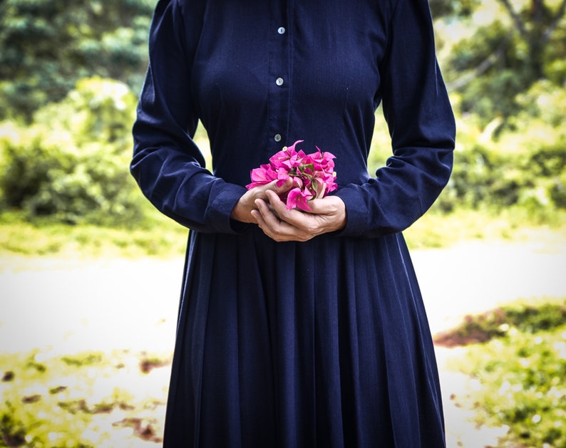 May include: A woman in a dark blue dress holds a bouquet of pink flowers in her hands.