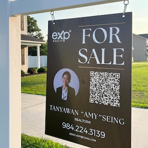 Op de afbeelding: Een zwart-wit onroerend goed bord met de tekst "COMING SOON" bovenaan. Het bord hieronder luidt "FOR SALE" en bevat een foto van een makelaar, een QR-code en contactgegevens.