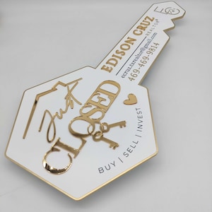 May include: A gold key-shaped sign with the words "Just Closed" in gold lettering. The sign also includes a small gold heart and two gold keys. The bottom of the sign reads "Buy | Sell | Invest" and includes the realtor's name and contact information: "Edison Cruz, Realtor, ecruz.txrealtor@gmail.com, 469-469-9814."