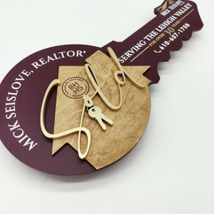 May include: A wooden key-shaped sign with the text "MICK SEISLOVE, REALTOR" and "SERVING THE LEHIGH VALLEY FOR OVER 30 YEARS - 610-657-1758". The sign is painted in shades of brown and burgundy.