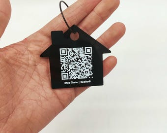 Op de afbeelding: Zwarte sleutelhanger in de vorm van een huis met een witte QR-code en de tekst "Erica Stone | Realtor®".