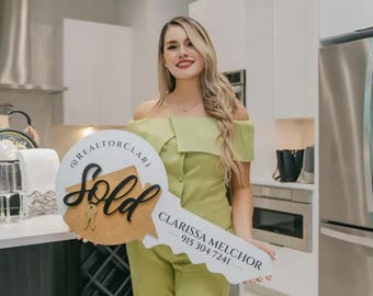 May include: A woman in a green outfit holds a large wooden key with the word "Sold" and the text "@REALTORCLARI  CLARISSA MELCHOR - 915 304 7241" on it.