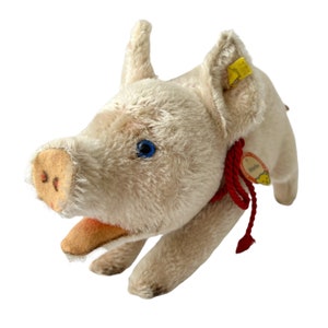 May include: A vintage white plush pig toy with blue eyes and a red ribbon around its neck. The toy has a yellow tag with the word "Steiff" on it.