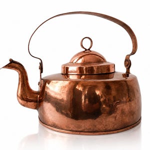 May include: A copper kettle with a curved spout, a hinged lid, and a large arched handle. The kettle has a polished finish, reflecting light. The design is classic and functional, suitable for stovetop use.