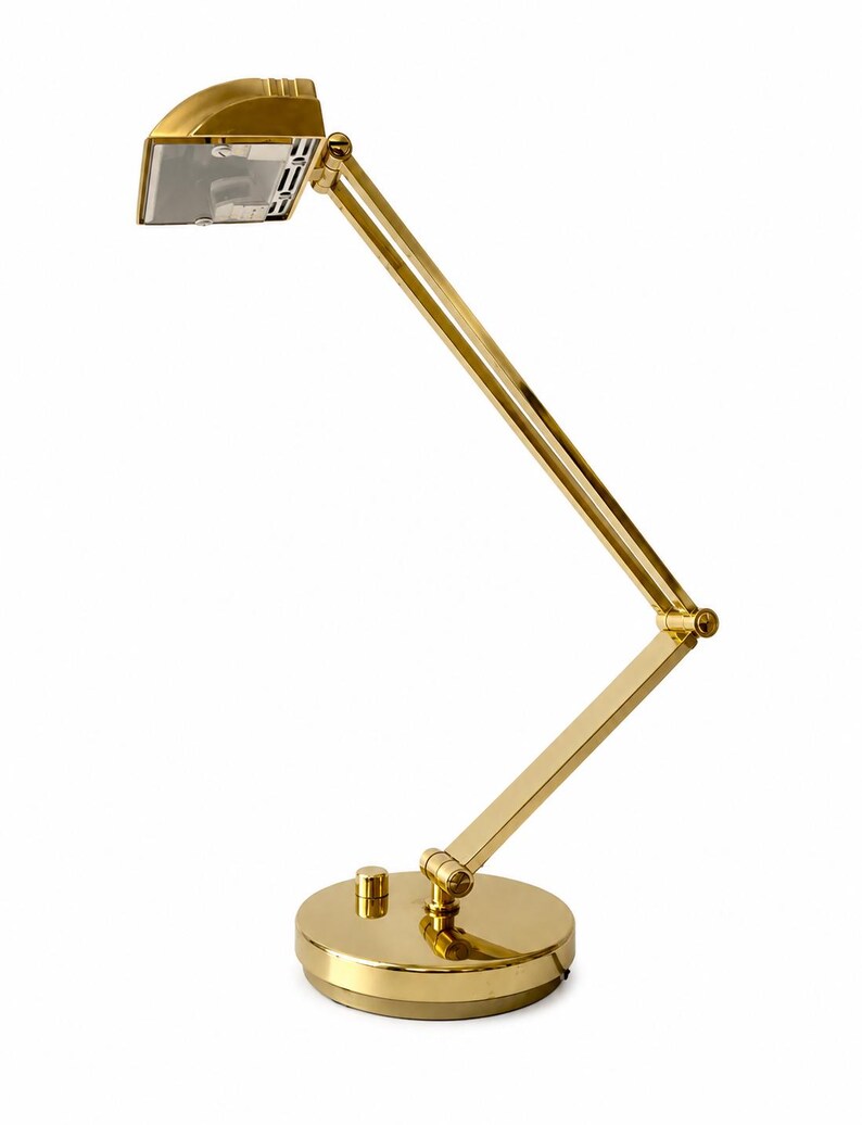 May include: A gold-colored desk lamp with an adjustable arm and a round base. The lamp has a rectangular light fixture and a small on/off switch on the base. The design is sleek and modern, suitable for a home office or study.