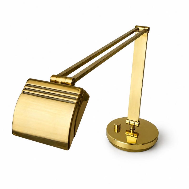 May include: A brass-colored desk lamp with an adjustable arm and shade. The lamp has a round base and a rectangular shade with horizontal lines. The design is reminiscent of vintage office lighting.