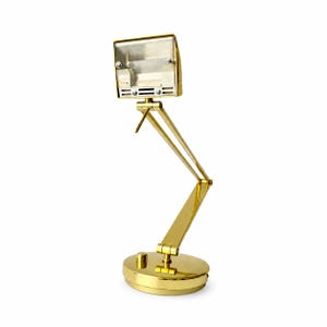 May include: A gold-colored desk lamp with a rectangular head and an adjustable arm. The lamp has a round base with a small button and a pivoting head. The lamp is made of metal and has a shiny finish.