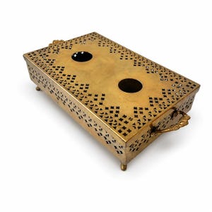 May include: A rectangular brass serving tray with decorative cut-out patterns and two circular openings. The tray has ornate handles and small feet, set against a white background.