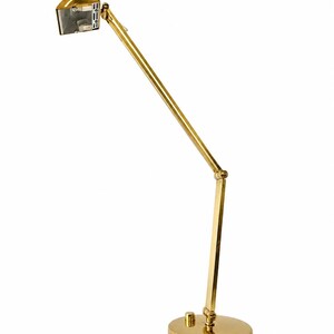 May include: A gold-colored desk lamp with an adjustable arm and a round base. The lamp has a rectangular head and a sleek, modern design. The lamp is made of metal and has a shiny finish.