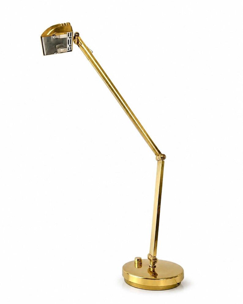 May include: A gold-colored desk lamp with an adjustable arm and a round base. The lamp has a rectangular head and a sleek, modern design. The lamp is made of metal and has a shiny finish.
