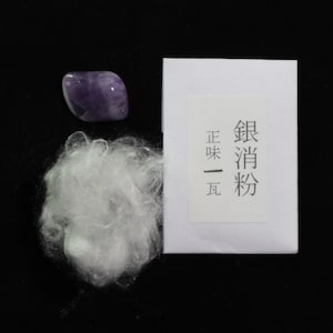 May include: A small purple amethyst crystal, a clump of white cotton filling, and a white card with the text "正味一瓦" and "銀箔" in black.