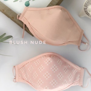 Op de afbeelding: Twee gezichtsmaskers. Het bovenste masker is blush nude, en het onderste masker is roze koraal kruisen. Beide maskers hebben verstelbare oorlussen. De merknaam "LOVELAFFCO" staat bovenaan de afbeelding.