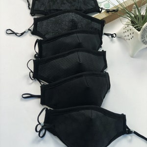 May include: A stack of five black face masks with different patterns. The masks are made of a soft, breathable fabric and have adjustable ear loops.