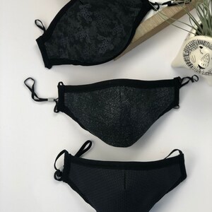 May include: Three black face masks with different patterns. The top mask has a floral pattern, the middle mask has a textured pattern, and the bottom mask has a mesh pattern.